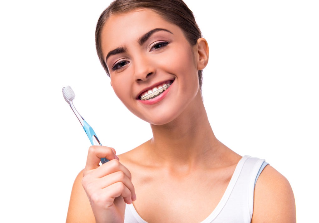 Portrait of a beautiful woman with braces on the teeth, cleans teeth with toothbrush, isolated on a white background